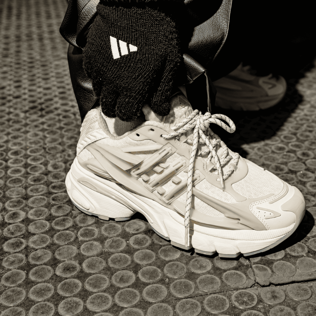 Close-up of a beige Adidas Adistar Jellyfish sneaker on a textured surface.