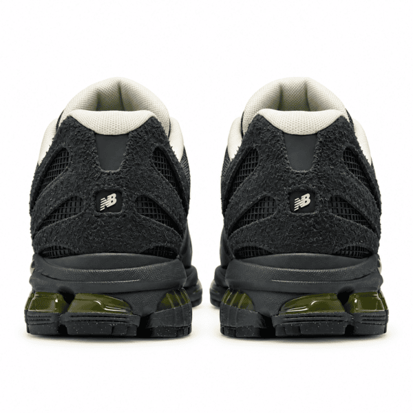 Black and beige New Balance sneakers with green sole details, rear view.