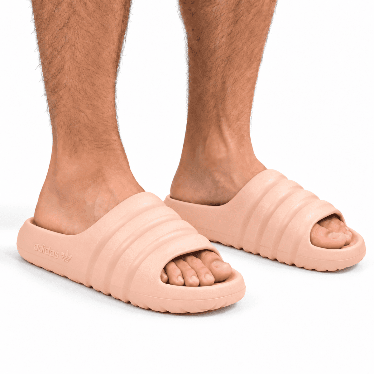 Light peach Adidas Adilette slides worn by a person with visible legs.