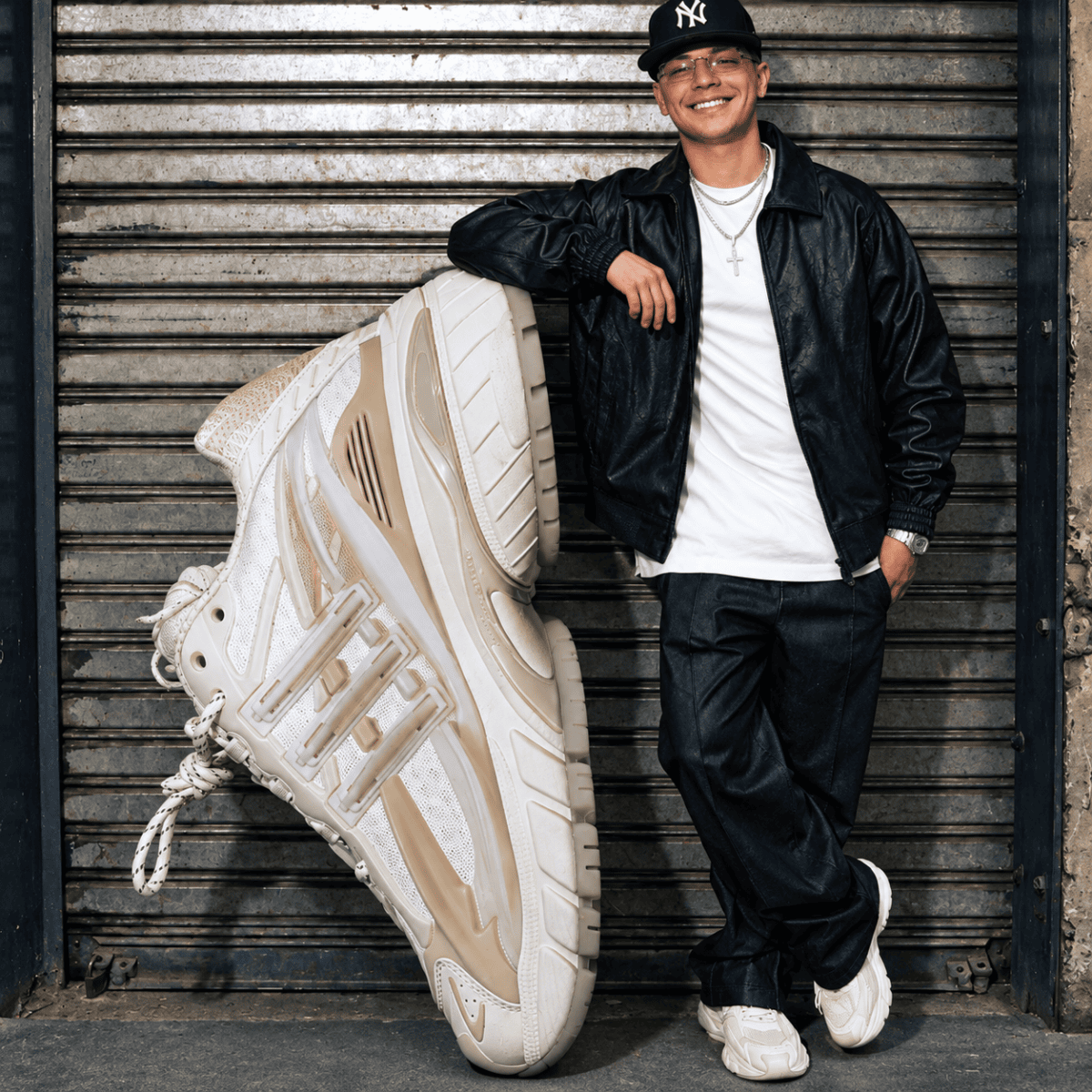 Young man in black jacket and white sneakers with oversized white sneaker in front.