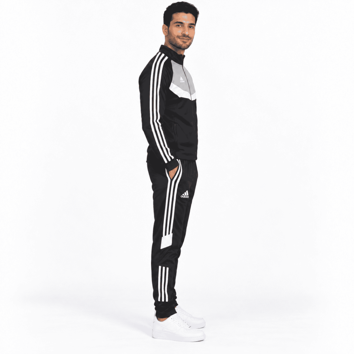 Man in black and white Adidas tracksuit with white sneakers, standing sideways.