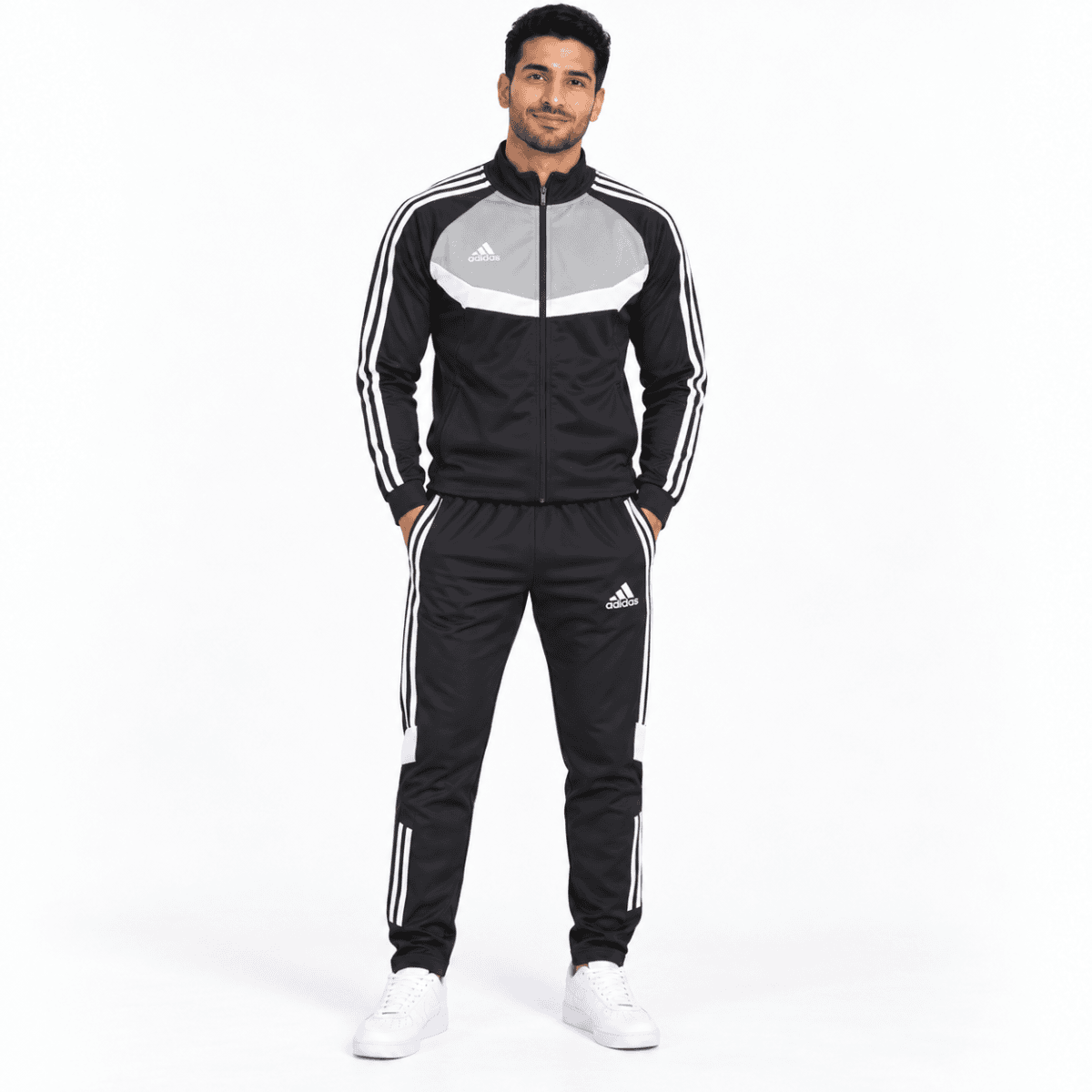 Man in black and grey Adidas tracksuit with white stripes, standing against white background.