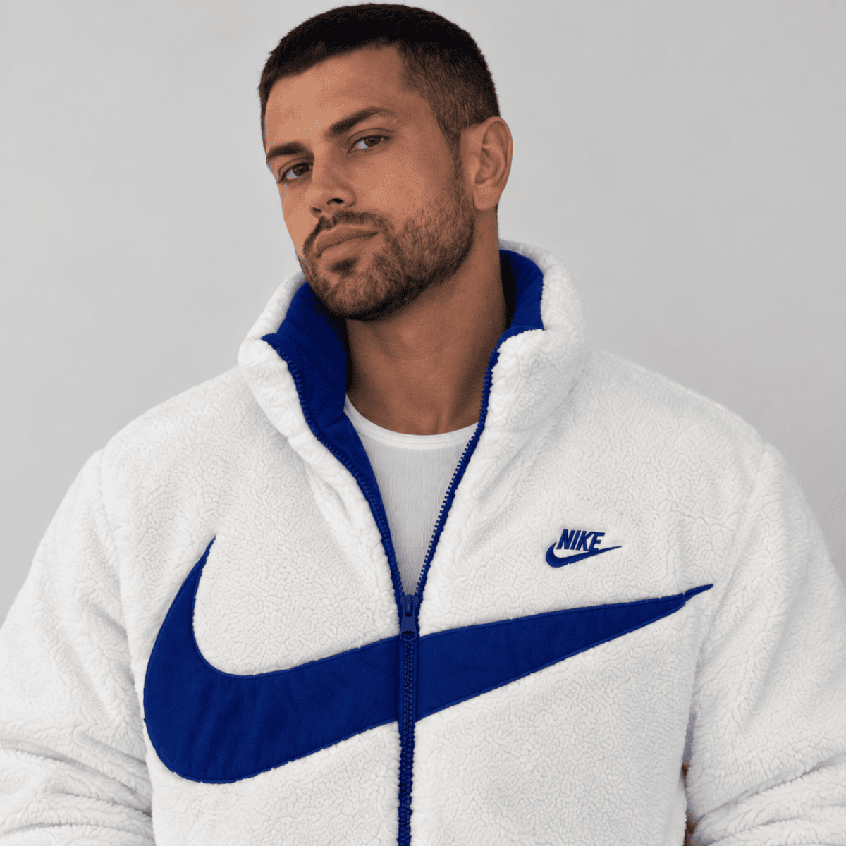 Man wearing white and blue Nike fleece jacket with large swoosh logo.