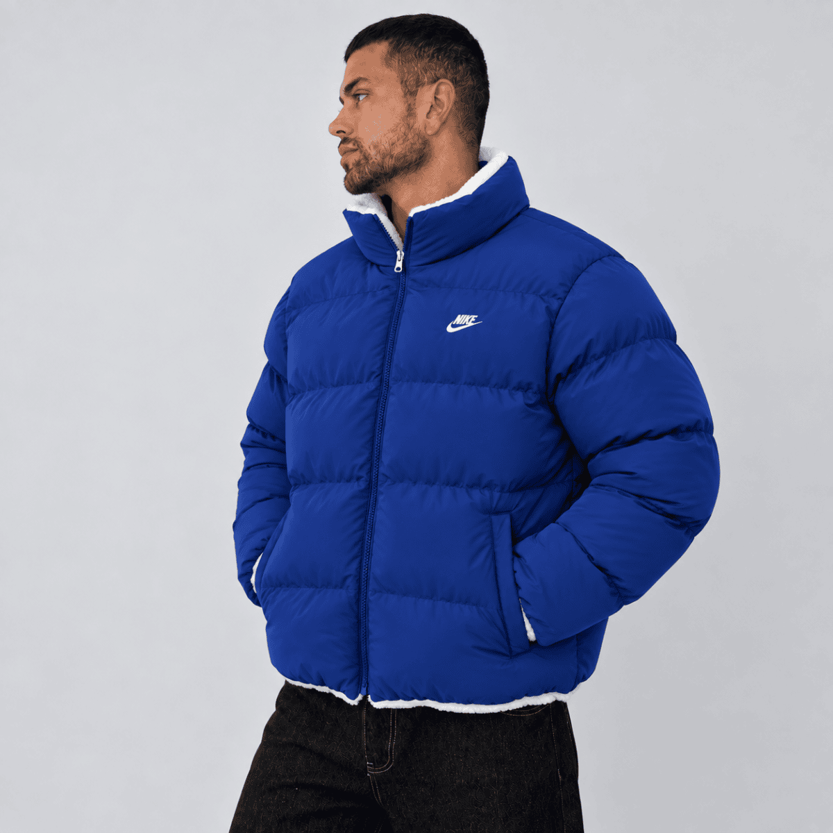 Man in blue Nike puffer jacket facing left against plain background.