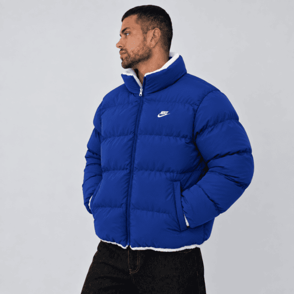 Man in blue Nike puffer jacket facing left against plain background.