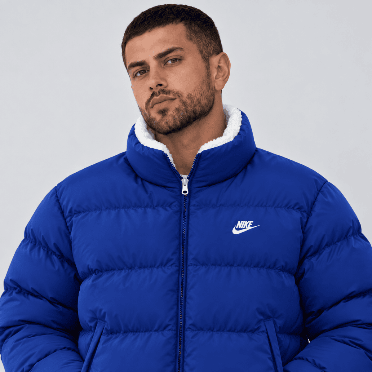 Man wearing a blue Nike puffer jacket with white logo and high collar.