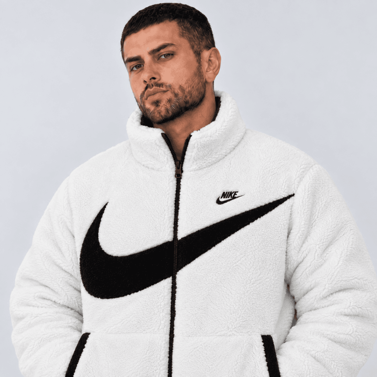 Man wearing white Nike fleece jacket with black swoosh logo, front view.