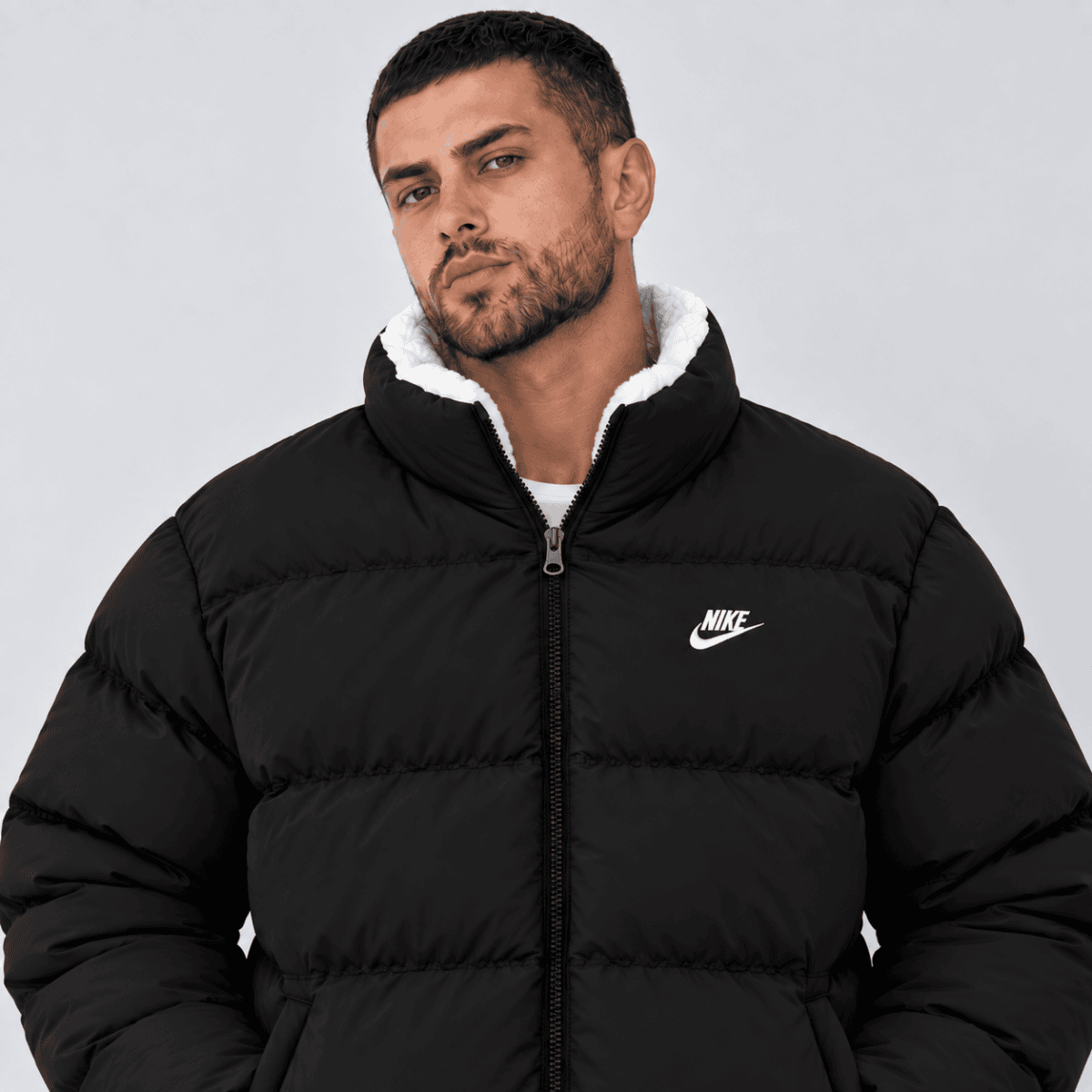 Man wearing black Nike puffer jacket with white lining, front view.