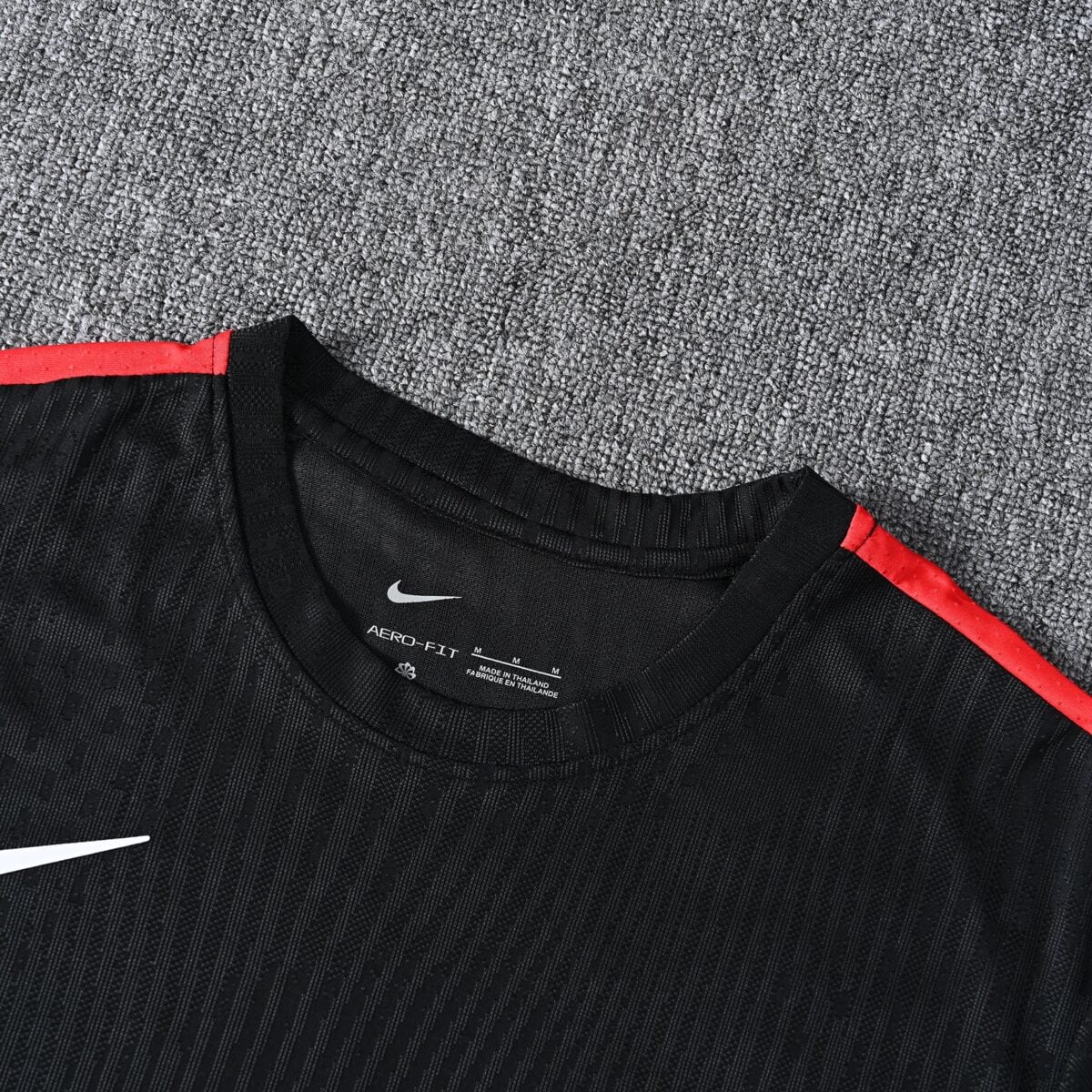 Close-up of black football jersey with red shoulder stripes and Nike logo.