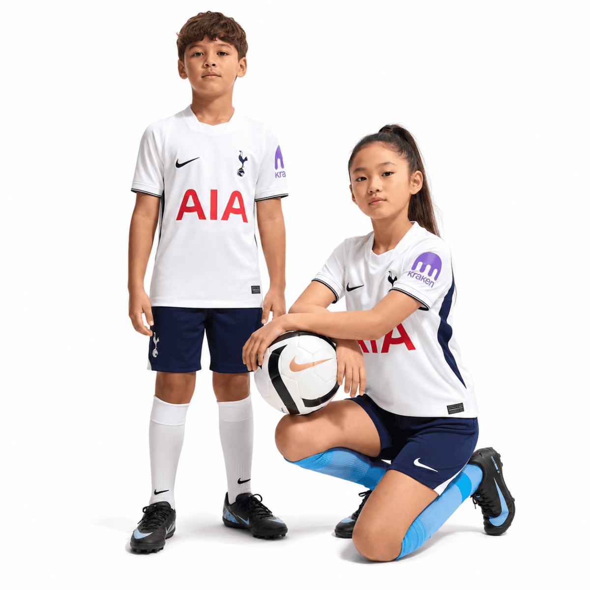 Two kids in Tottenham home football kits, one standing and one kneeling with a ball.