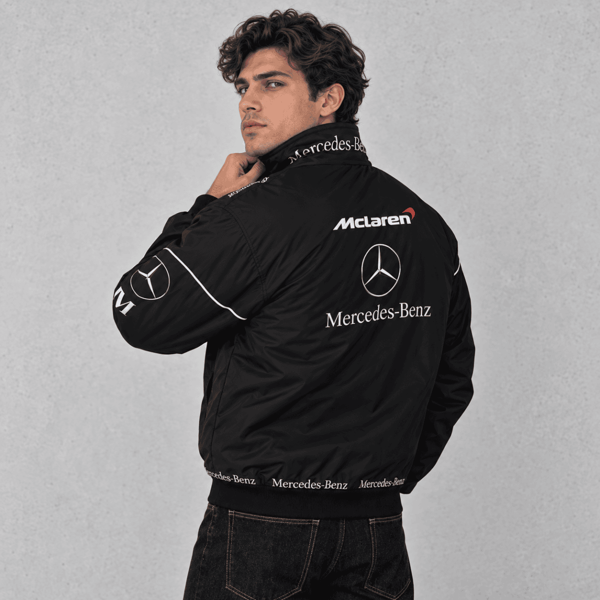 Man wearing black Mercedes-Benz branded jacket, back view, in a studio setting.