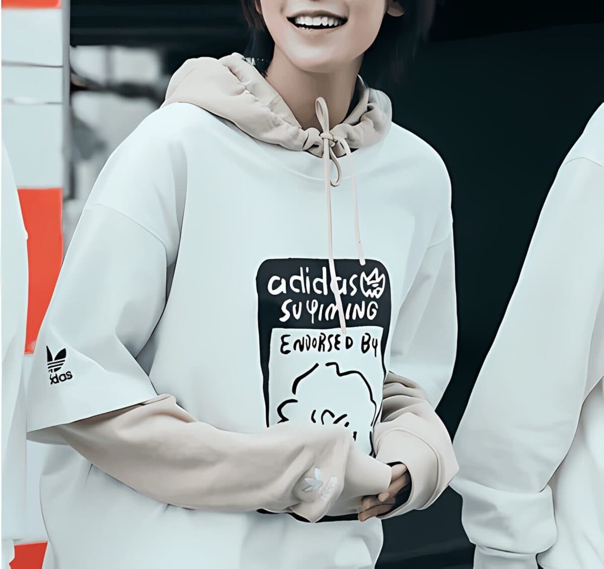 Person wearing a white Adidas hoodie with beige sleeves and graphic print.
