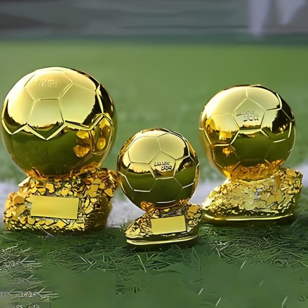 Three golden Ballon d'Or trophies on a green field.