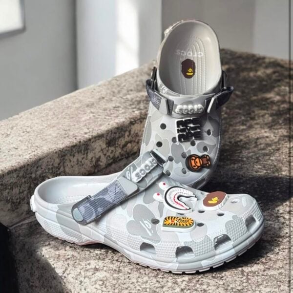 d36957fb-6b7a-4aec-9128-9ee32a35f1ec - UAE SPORT STORE BAPE x Crocs Classic Clog in grey camouflage with patches and straps.