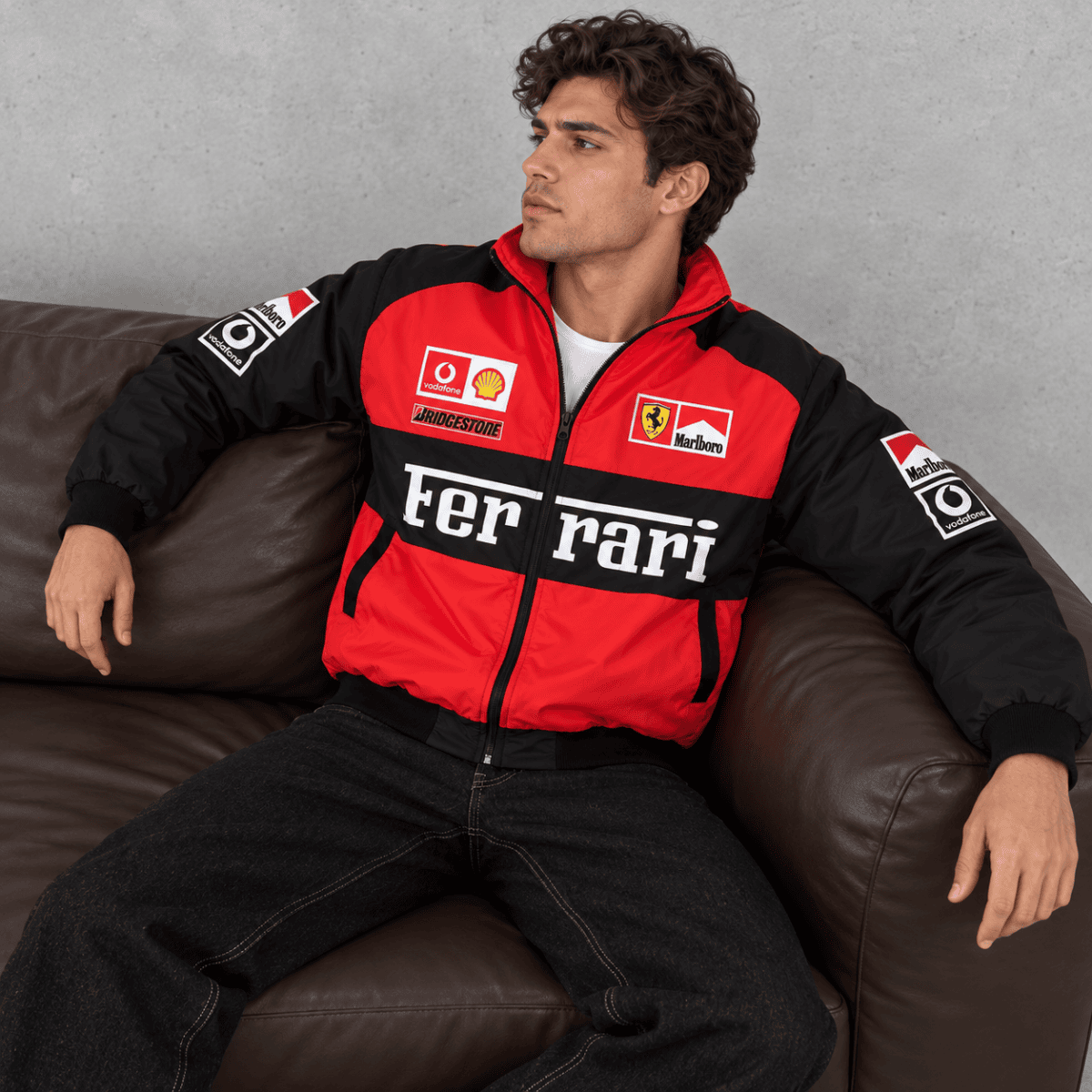 Man wearing Ferrari Formula 1 team jacket with sponsor logos, sitting on a brown sofa.