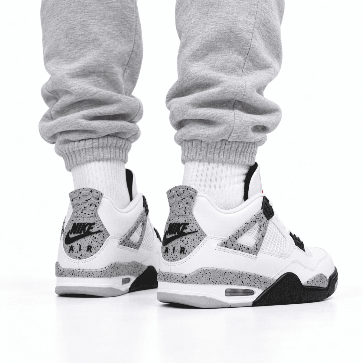 Person wearing white Nike Air Jordan 4 Retro OG sneakers with black and grey speckled details.