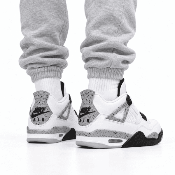 Person wearing white Nike Air Jordan 4 Retro OG sneakers with black and grey speckled details.