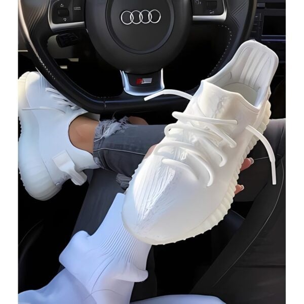 White athletic sneakers held in a car with a steering wheel in the background.