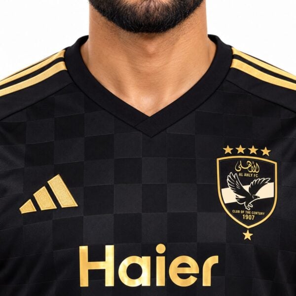 Al Ahly away jersey close-up of the metallic gold crest with four stars and the gold trimmed V-neck