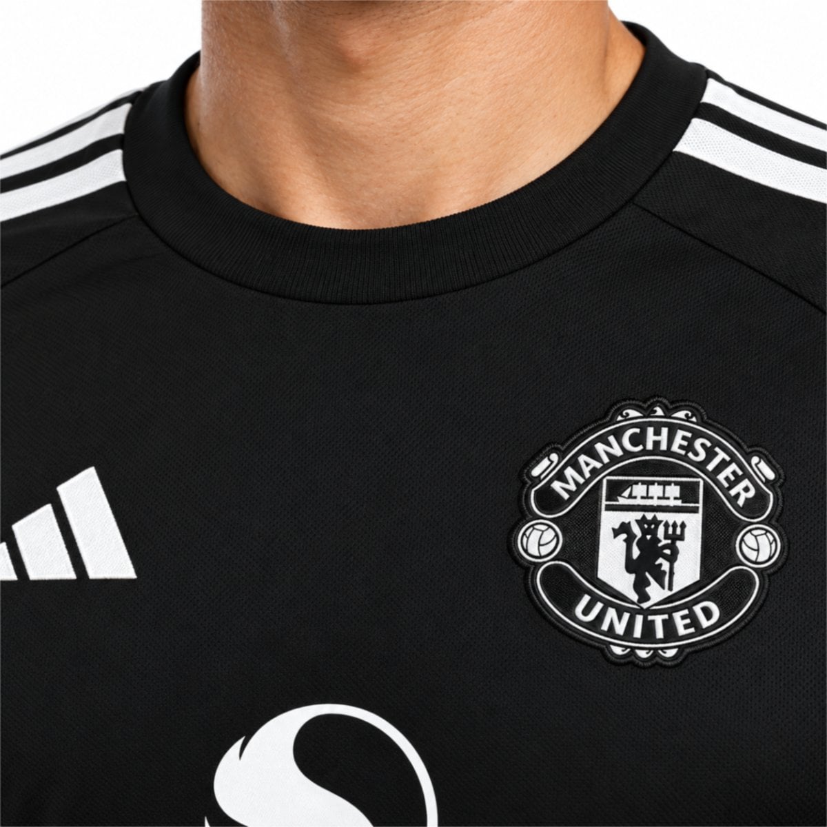 Manchester United goalkeeper jersey close-up of black and white embroidered crest and ribbed collar - UAE SPORT STORE Chest close-up of the black Manchester United shirt with white lettering and grey patterns.