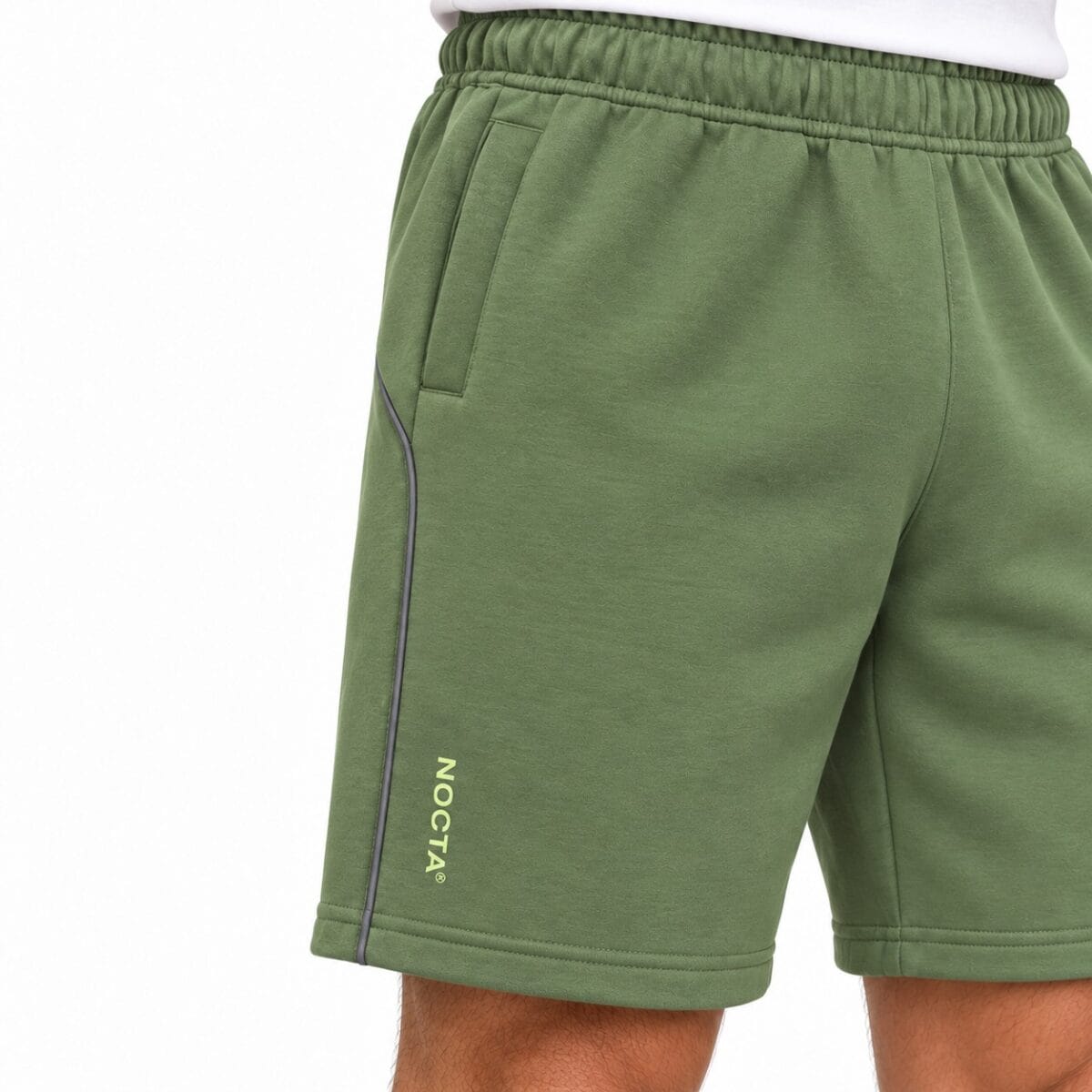 Green sports shorts with NOCTA logo and black piping detail.