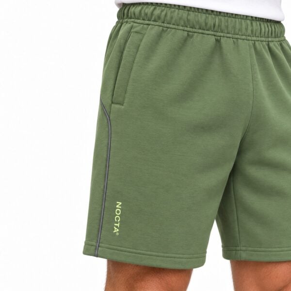 Green sports shorts with NOCTA logo and black piping detail.