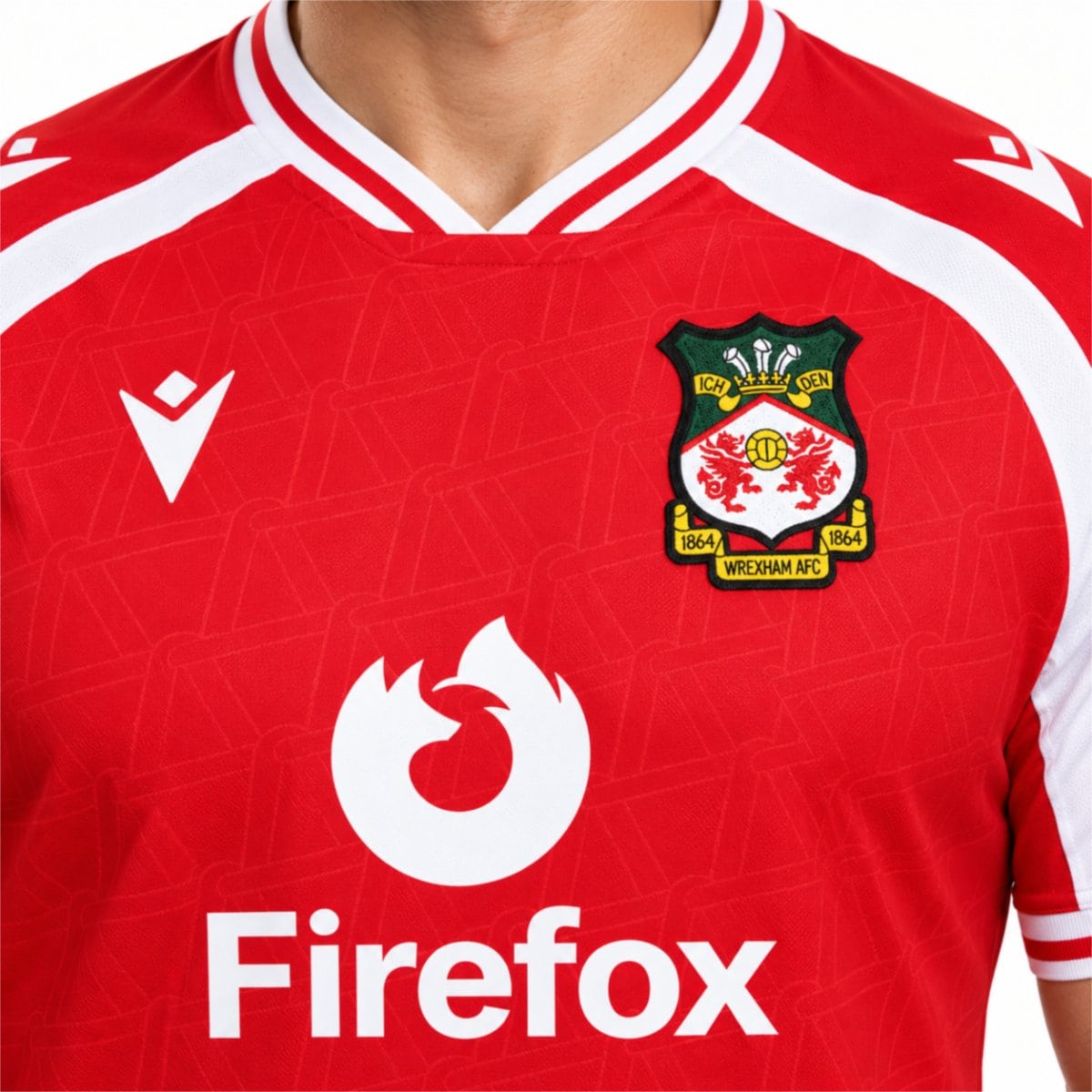 Wrexham home jersey close-up of the embroidered 1864 club crest and white shoulder panel - UAE SPORT STORE Chest close-up of the red Wrexham shirt with white Firefox lettering and sleeve trim.